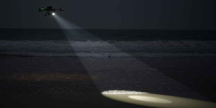 Drona Matrice 350 survolează noaptea pe o plajă și luminează valurile pe nisip la marginea malului cu DJI Zenmuse S1