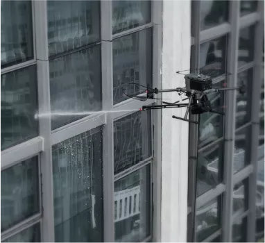 Sistemul Orion AP3-P3 de curățat clădiri care stropește cu jet puternic geamurile unei clădiri de birouri, montată pe o dronă DJI Matrice 350 RTK